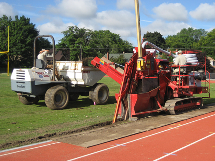 Laser-controlled trencher alongside running track, installing collector for slit drain system.